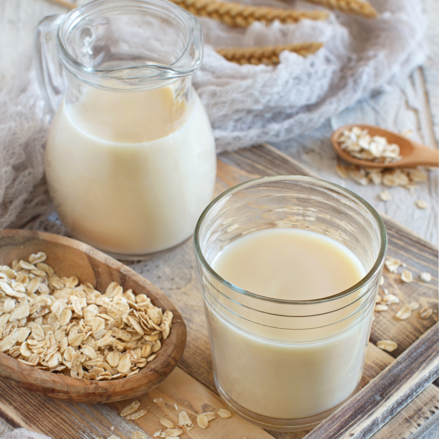 Hafermilch im Glas und in einer Karaffe daneben Haferflocken im Schälchen