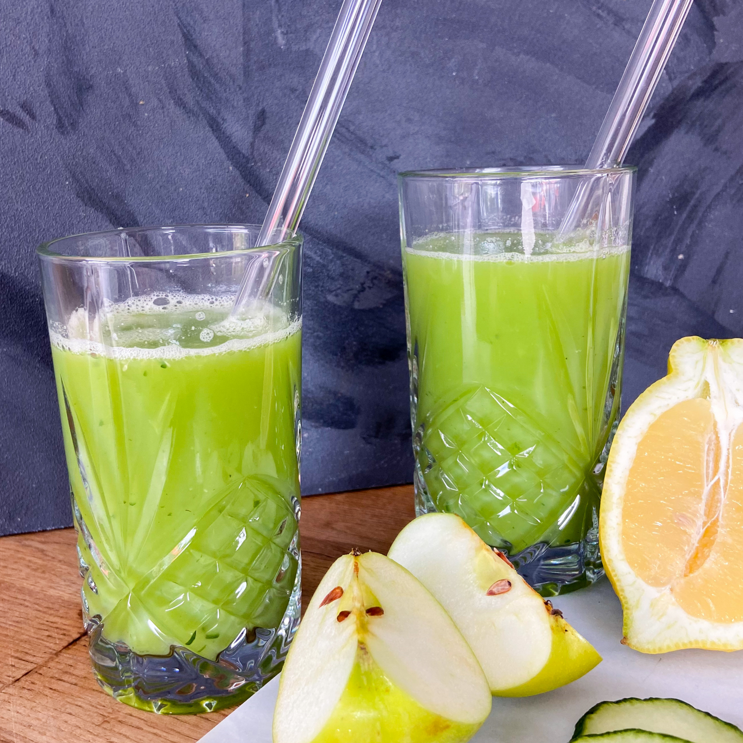 Zwei Gläser gefüllt mit Green Glow davor liegen die Zutaten für den Saft.