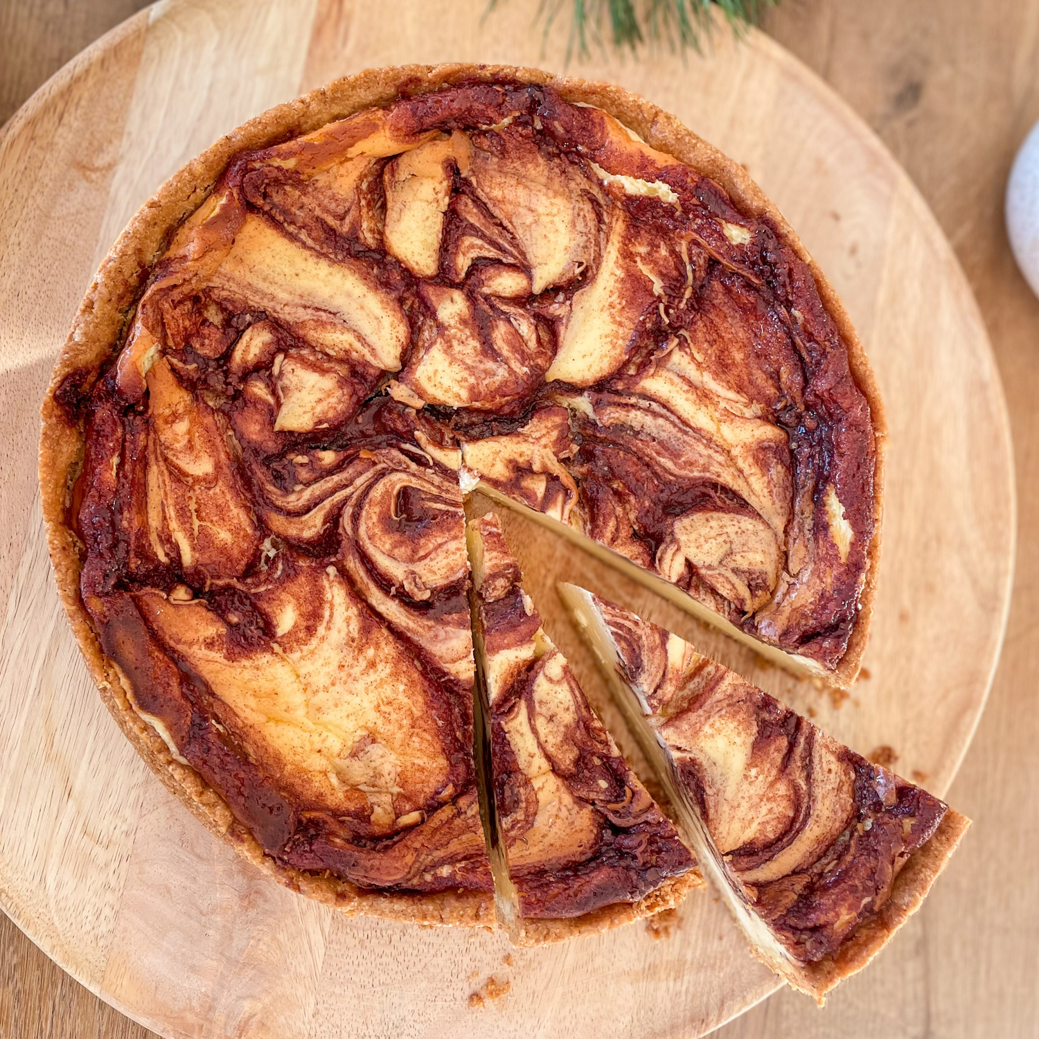 Mamorisierter Cinnamonrool-Cheesecake auf einem runden Holzbrett von oben.