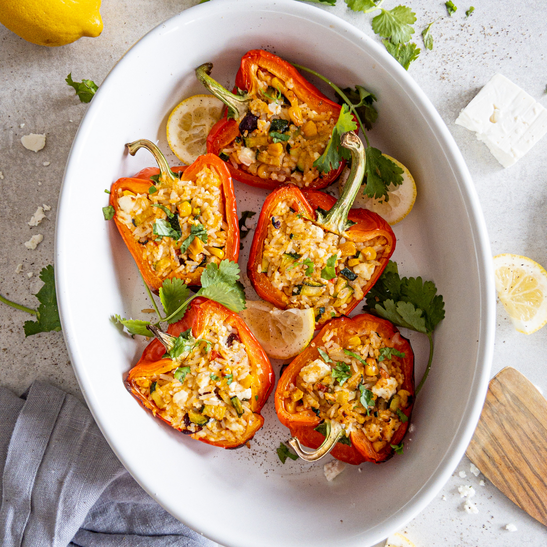 Gefüllte Paprikahälften in einer Auflauform zusammen mit Zitrone und Petersilie.