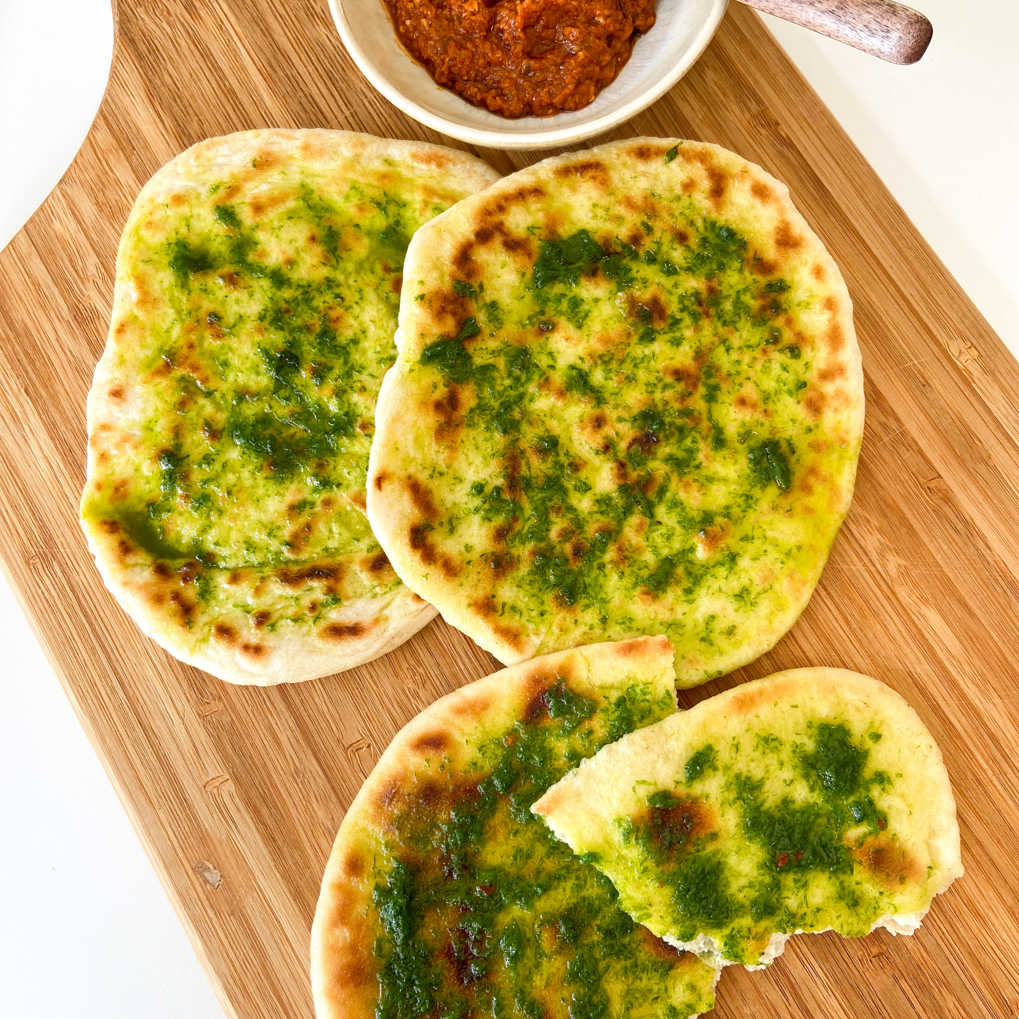 Drei Grill-Fladenbrote mit Kräuterbutter auf einem Holzbrettchen.