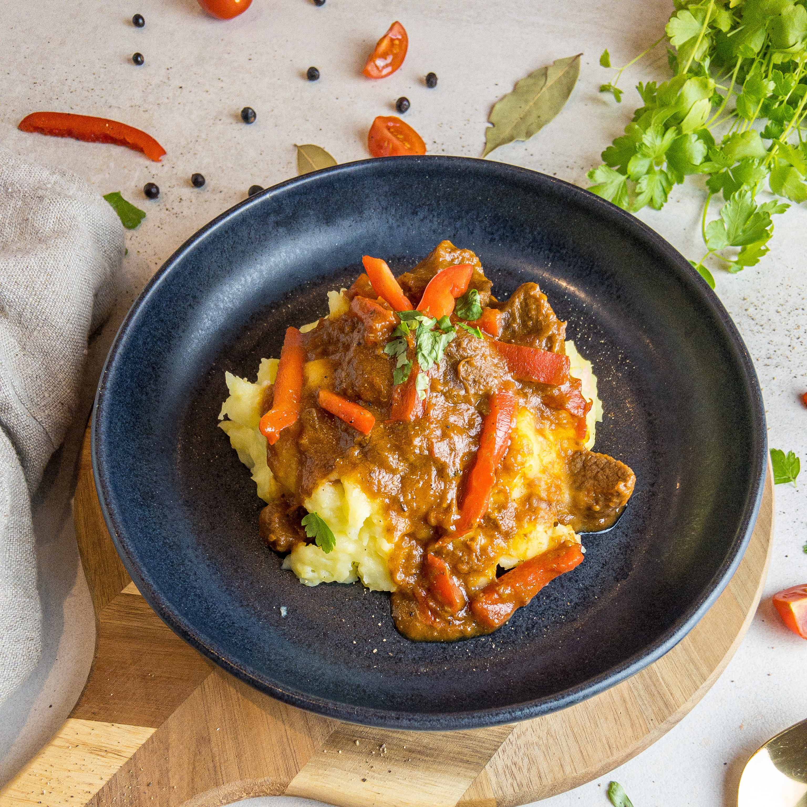 Kartoffelstampf mit Gulasch angerichtet auf einem dunklen Teller.