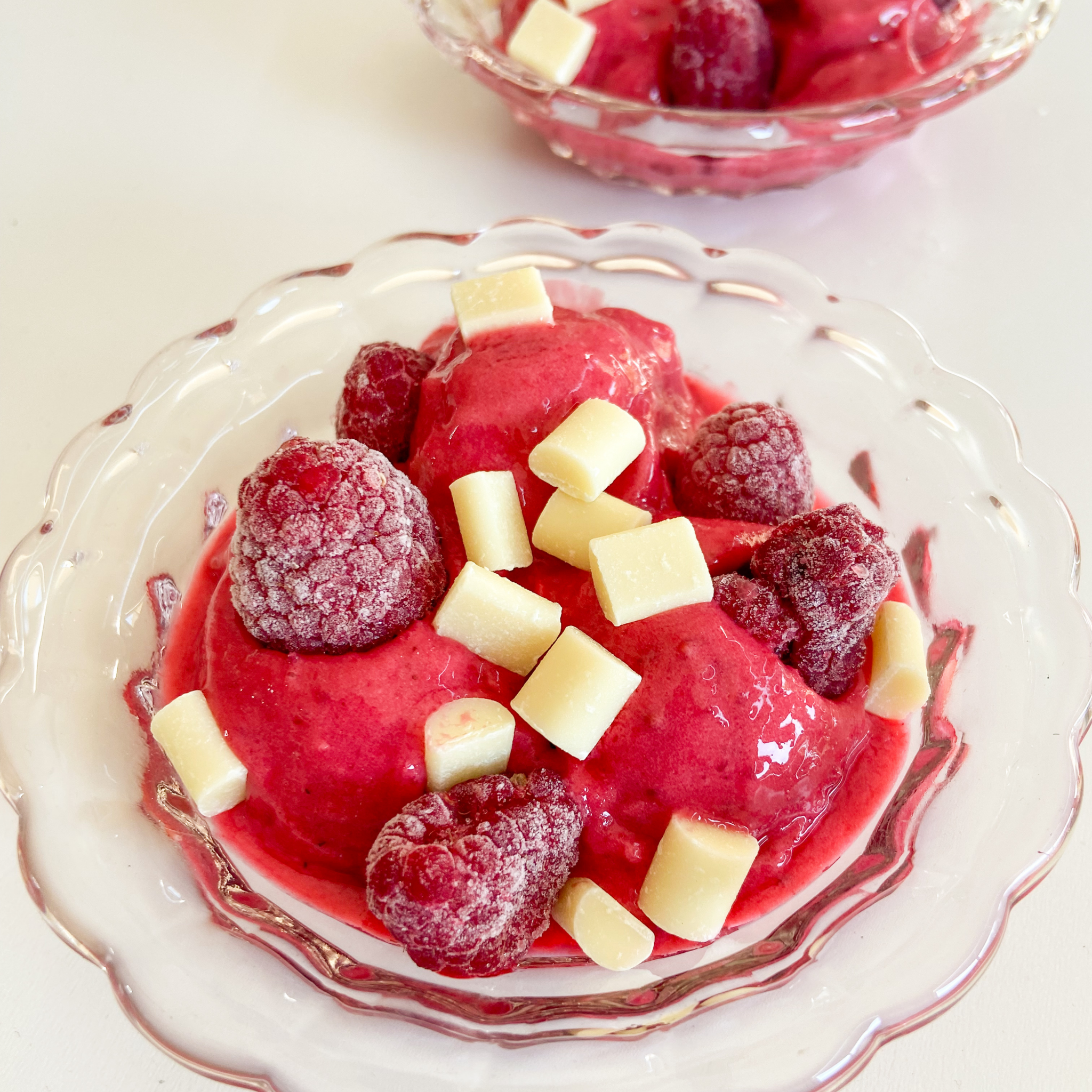 Himbeer-Blitzeis angerichtet in einer Schale mit TK-Himbeeren und weißen Schokostückchen.