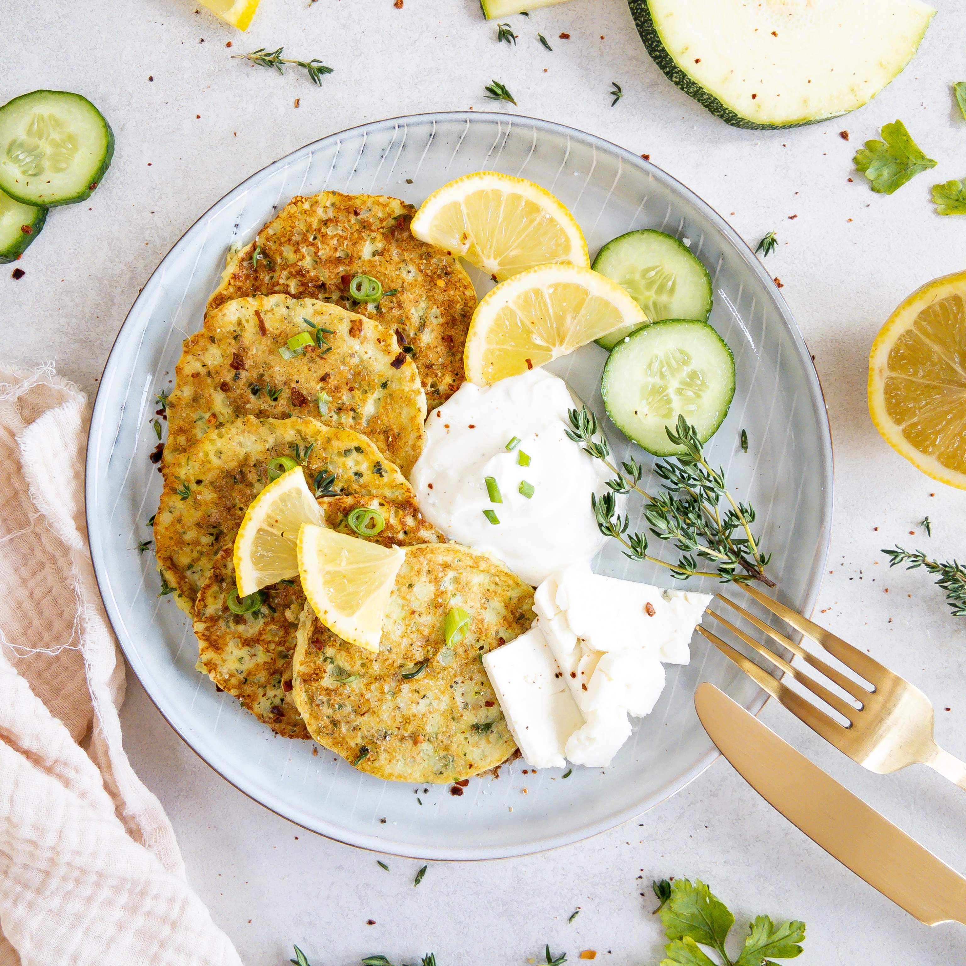 Zucchinipuffer zusammen mit Dip und etwas Feta auf einem Teller angerichtet.