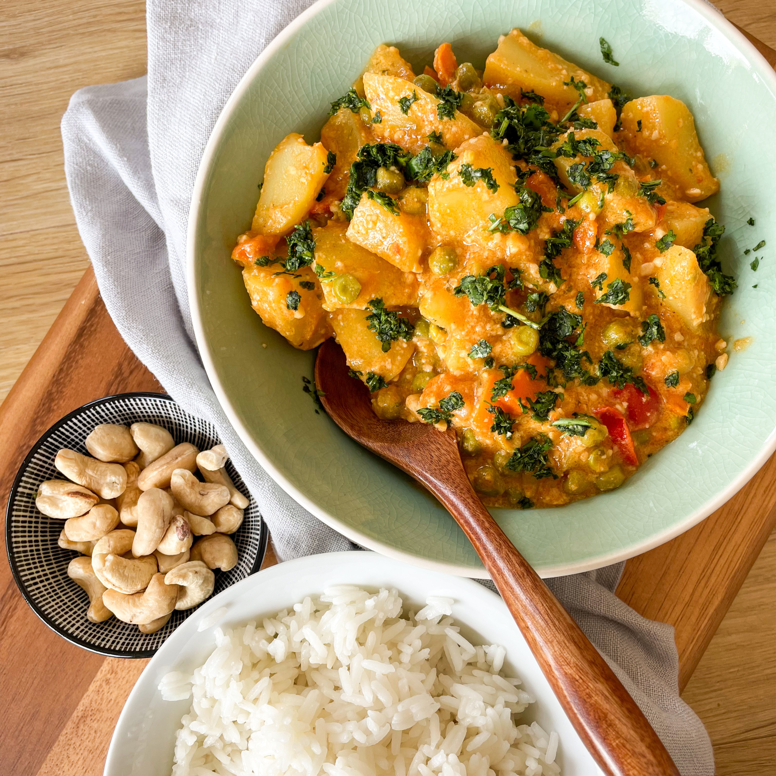Indisches Gemüse-Korma in einer Schüssel daneben eine Schale mit Reis und ein paar Cashewkerne.