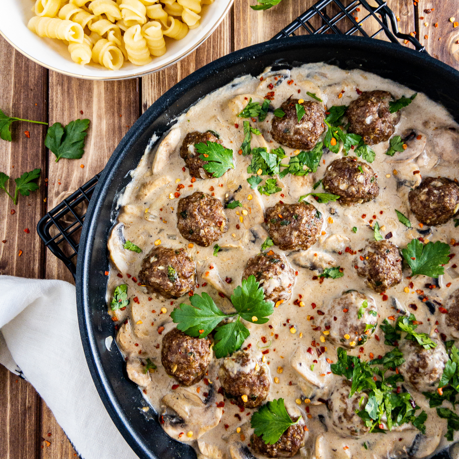 Köttbullar mit Pilzrahmsauce in einer Pfanne auf einem Holztisch.