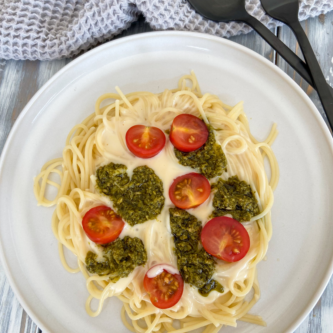 Spaghetti mit cremiger Käsesauce etwas Pesto und halbierten Kirschtomaten auf einem Teller angerichtet.