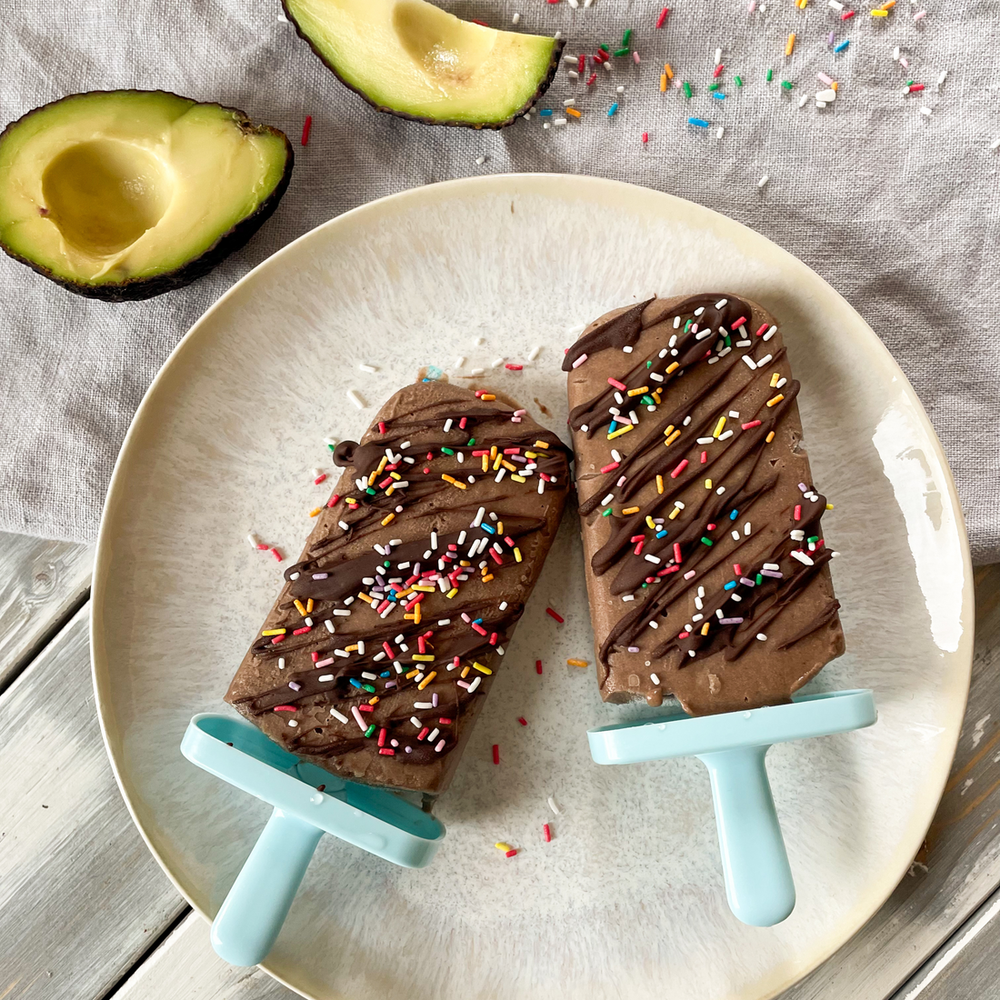 Zwei Schoko-Kokos Eis mit bunten Streuseln am Stiel liegend auf grauem Teller