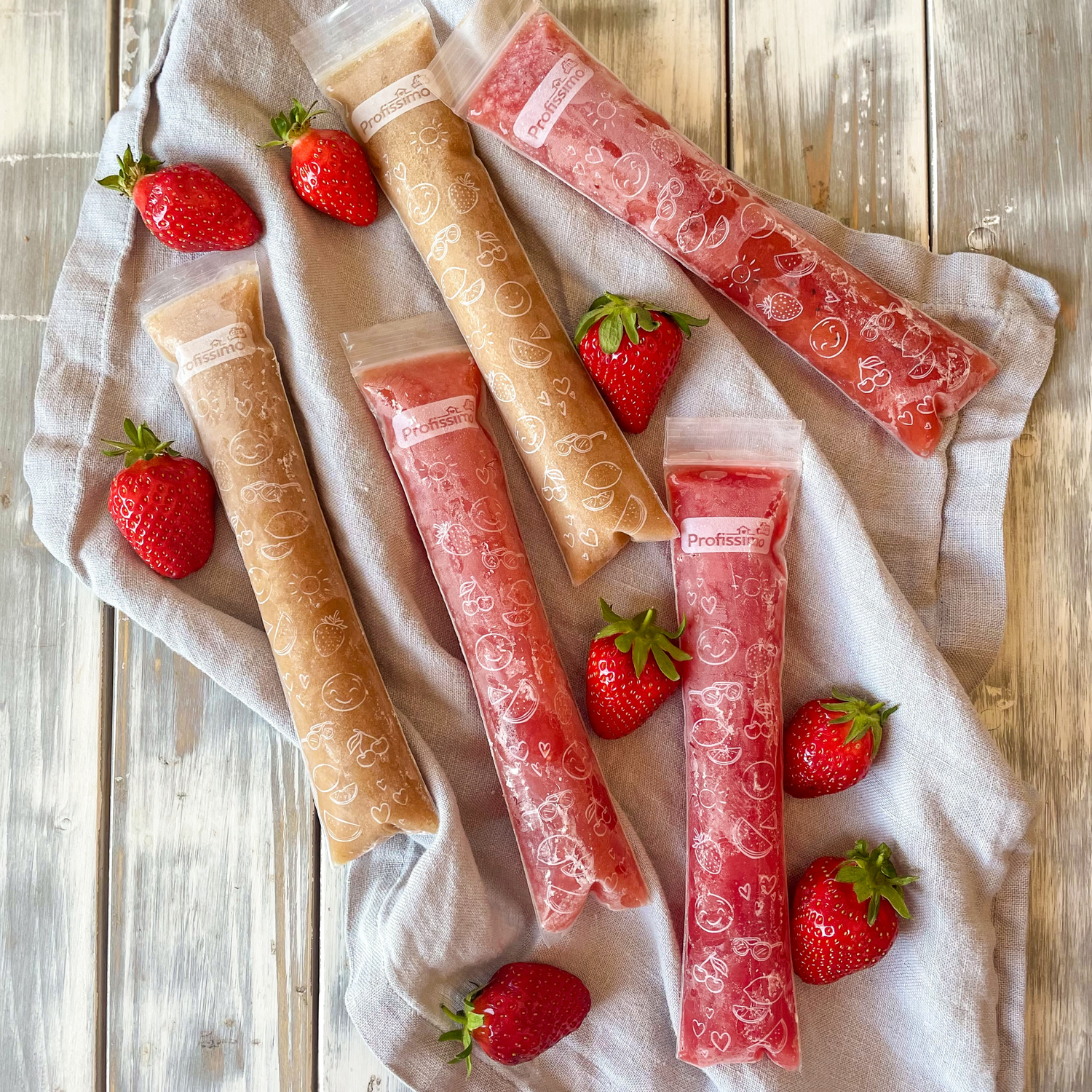Fünf Tütchen Wassereis liegend auf einem Tuch drumherum frische Erdbeeren