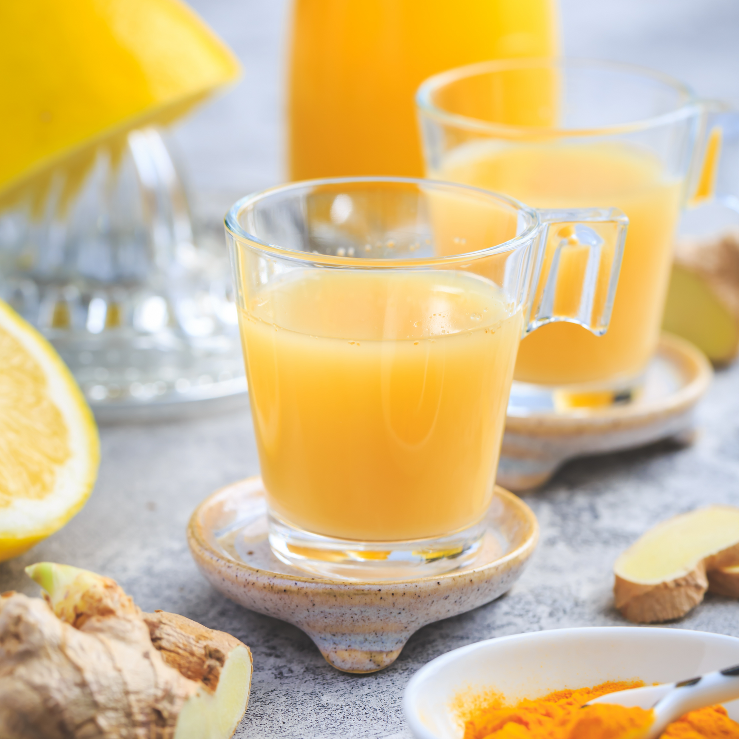 Zitrone-Ingwershot im Glas und drumherum aufgeschnittene Zitrone und Ingwer und Kurkumapulver im Schälchen.