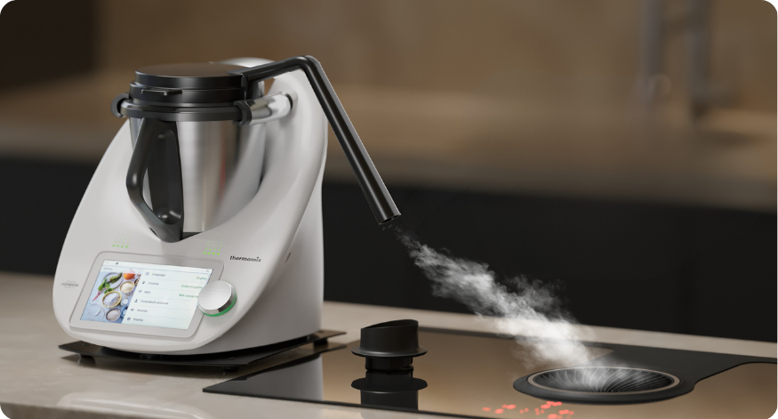 Thermomix auf einer Küchenarbeitsfläche, der mit einem Dampfumleiter ausgestattet ist, der den Dampf gezielt in ein Abluftsystem auf dem Kochfeld ableitet.